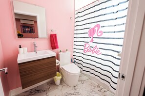 Een badkamer met een roze muur, een wit wastafel, een houten opbergmeubel, een wit toilet en een gestreept douchegordijn met de tekst 'Baby'.