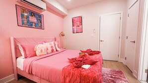 Ein zartrosa Schlafzimmer mit Bett, Kissen und einem Poster an der Wand.