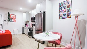Eine moderne Küche mit weißen Schränken, einem Edelstahl-Kühlschrank und einem Essbereich mit weißem Tisch und rosa Stühlen.
