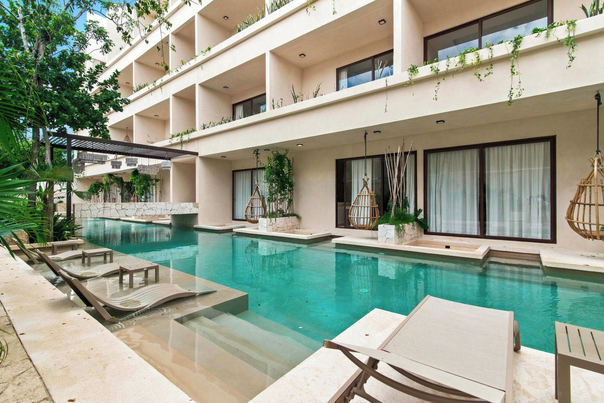 A hotel with a swimming pool, lounge chairs, and a pergola with plants.