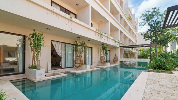 Ein modernes Hotel mit Schwimmbad, Sitzgelegenheiten im Freien und üppiger Bepflanzung.
