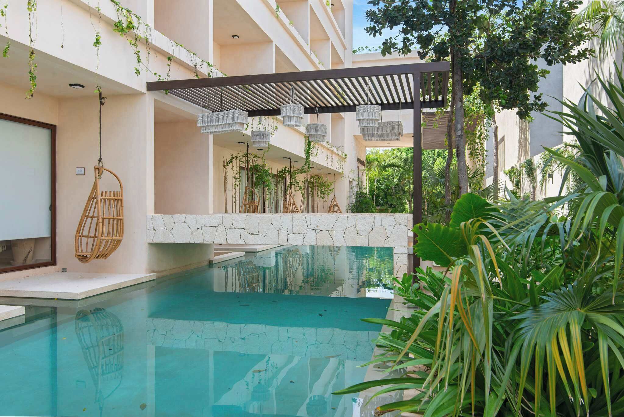 A pool area with a clear blue pool, a hanging chair, and lush greenery.