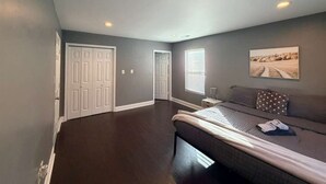 Een slaapkamer met een groot bed, een nachtkastje, een raam met zonwering en een deur naar een andere kamer.