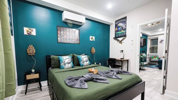 Ein modernes Schlafzimmer mit türkisfarbenen Wänden, einem großen Bett mit grüner Bettwäsche und Philadelphia Eagles Dekoration.