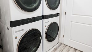 A laundry room with two stacked front-loading washing machines and a blue detergent container. - Superhero Stay Marvel Fan Paradise. (Philadelphia)