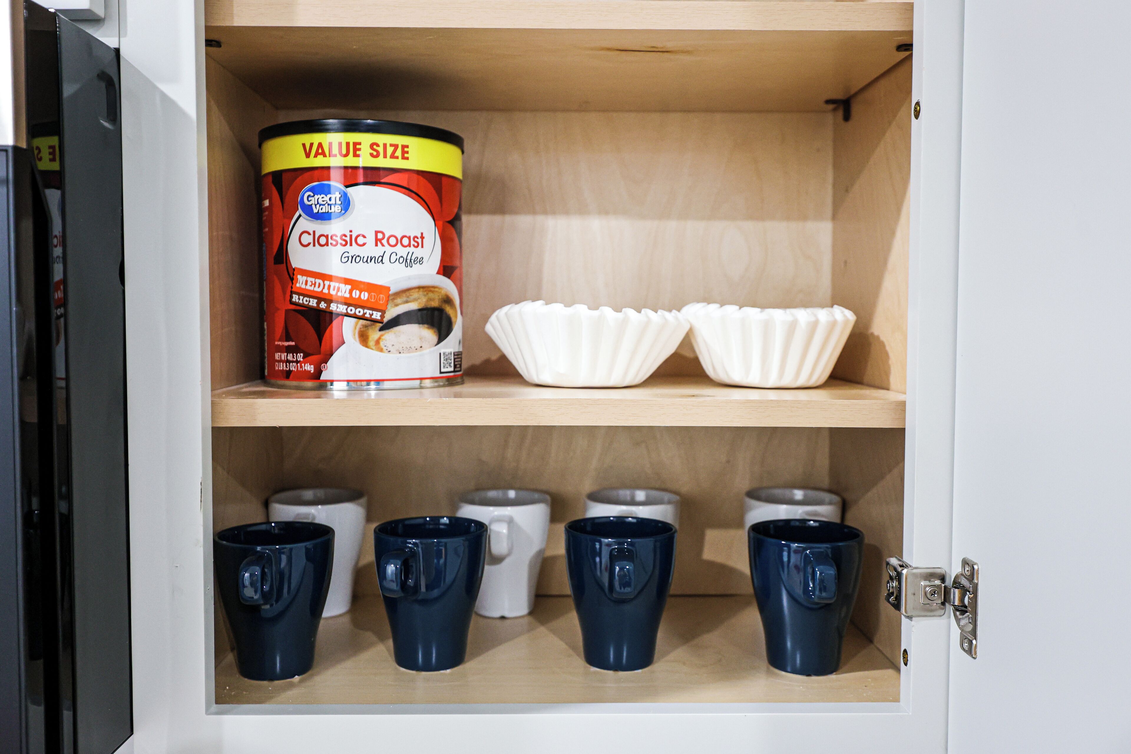 A cabinet with a coffee can, paper cups, and a coffee pot.
