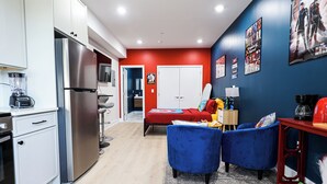 A compact living space with a kitchenette, a bed with red bedding, and a blue armchair. - Superhero Stay Marvel Fan Paradise. (Philadelphia)