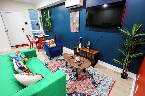 A living room with a green sofa, a blue armchair, a wooden coffee table, and a red rug. - Superhero Stay Marvel Fan Paradise. (Philadelphia)