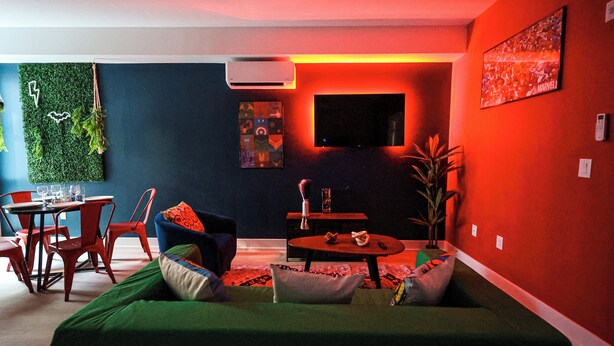 Un salon moderne avec un canapé vert, des fauteuils rouges, une petite table ronde et un téléviseur à écran plat fixé au mur.