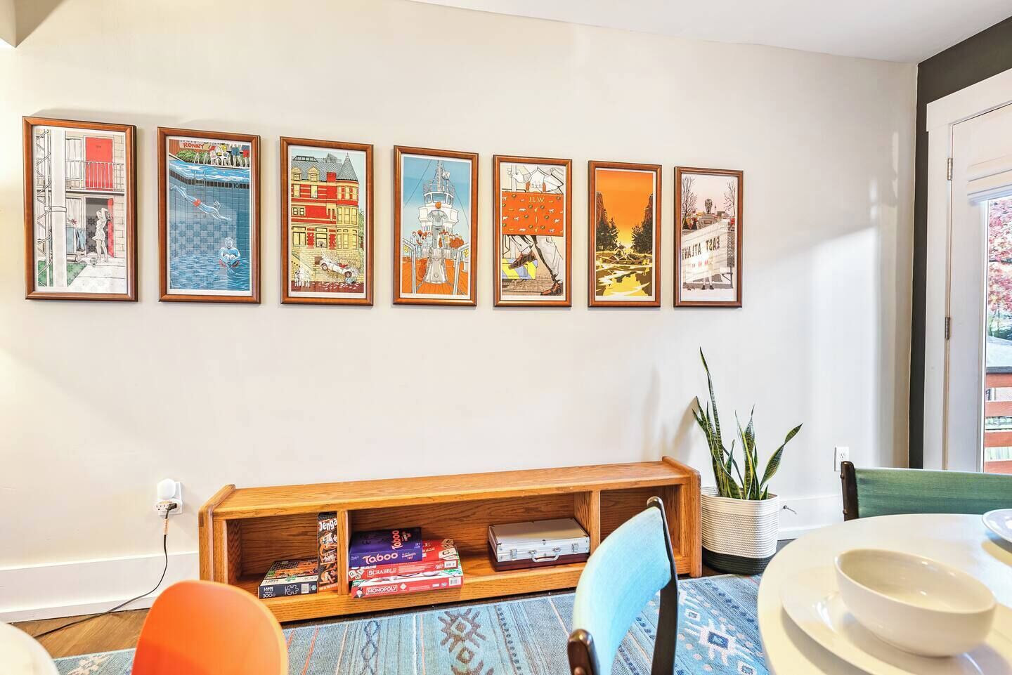 Un salon avec une bibliothèque, un coin repas comprenant une table et des chaises, et un mur orné de six œuvres d’art encadrées.