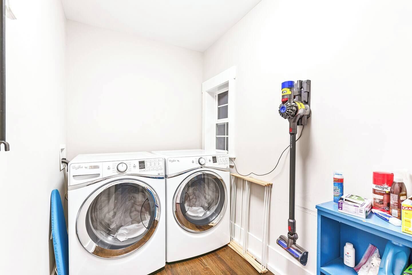 A laundry room with two front-loading washing machines, a drying rack, and a vacuum cleaner.