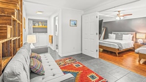 Ein kompakter Wohnraum mit Sofa, Bett, Küchenzeile und Deckenventilator.