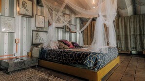 Ein Schlafzimmer mit Baldachinbett, gerahmten Kunstwerken an den Wänden und einer sichtbaren Steckdose.