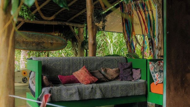 Ein grünes Sofa mit gemusterten Kissen in einem überdachten Außenbereich mit einem Reetdach und hängenden Dekorationen.