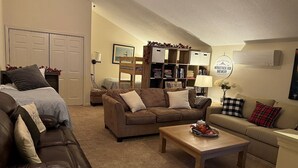 Una sala de estar acogedora con un sofá de cuero marrón, un sofá beige, una mesa de centro de madera y una estantería.