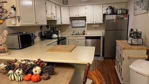 Una cocina con armarios blancos, microondas, refrigerador y una mesa de comedor de madera con calabazas.
