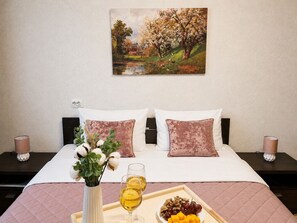 A hotel room with a bed, two bedside tables, a painting on the wall, a vase with flowers, and a tray with food and drinks. - Apartment near Komarovsky Market (Minsk)