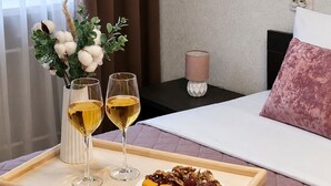 A tray with two glasses of white wine, a plate of cheese and grapes, and a vase with cotton plants on a wooden table in a room with a bed and a nightstand. - Apartment near Komarovsky Market (Minsk)