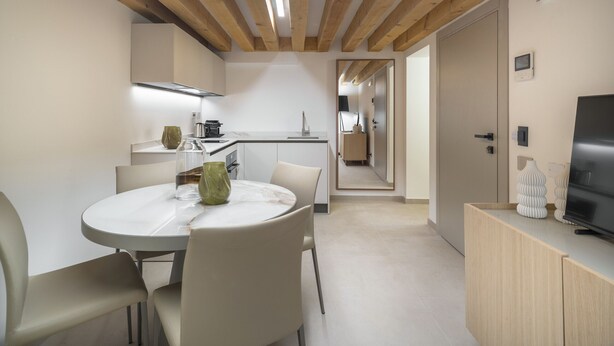Una cocina moderna con vigas de madera, un comedor con una mesa redonda y sillas, y un televisor sobre un mueble de madera.
