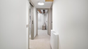 Un pasillo estrecho con un radiador, una puerta que da a un baño y una lámpara en el techo.