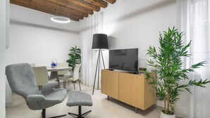 A modern living room with a grey armchair, a wooden TV stand, a floor lamp, and a large bamboo plant. - Palace Of The Elect Blue Apartment R&R (Venecia)