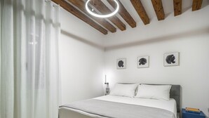 A modern bedroom with a bed, white curtains, wooden beams, and three black-and-white framed pictures on the wall. - Palace Of The Elect Blue Apartment R&R (Venecia)
