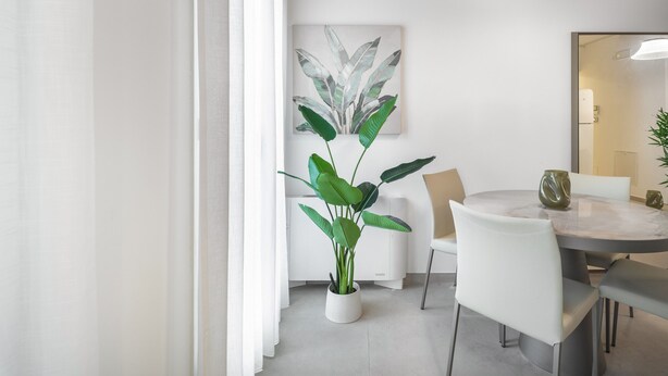A modern dining area with a round table, white chairs, a potted plant, and a wall-mounted light fixture. - Palace Of The Elect Green Apartment R&R (Venecia)