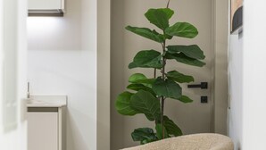 Una habitación moderna y minimalista con un sillón y reposapiés color beige, una planta verde grande y una puerta con manija.