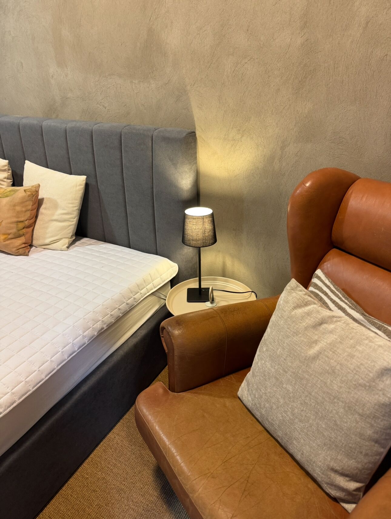 A bedroom with a bed, a nightstand, a lamp, and a leather armchair.