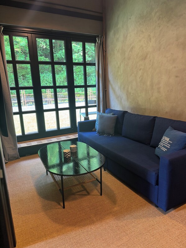 Una habitación con un sofá azul, una mesa de centro de cristal y vistas a zonas verdes a través de amplios ventanales.