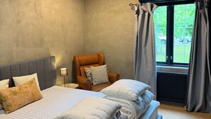Et soveværelse med en stor seng, en stol, et vindue med gardiner og en radiator.