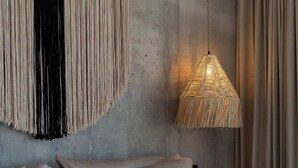 En seng med puder, et makramvægophæng og en hængende lampe.