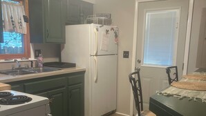 A kitchen with green cabinets, a white refrigerator, a stove, a dining table with chairs, and a window with blinds.