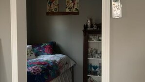 A bedroom with a bed, floral bedspread, two wall-mounted paintings, a bedside table with a lamp, and a telephone.