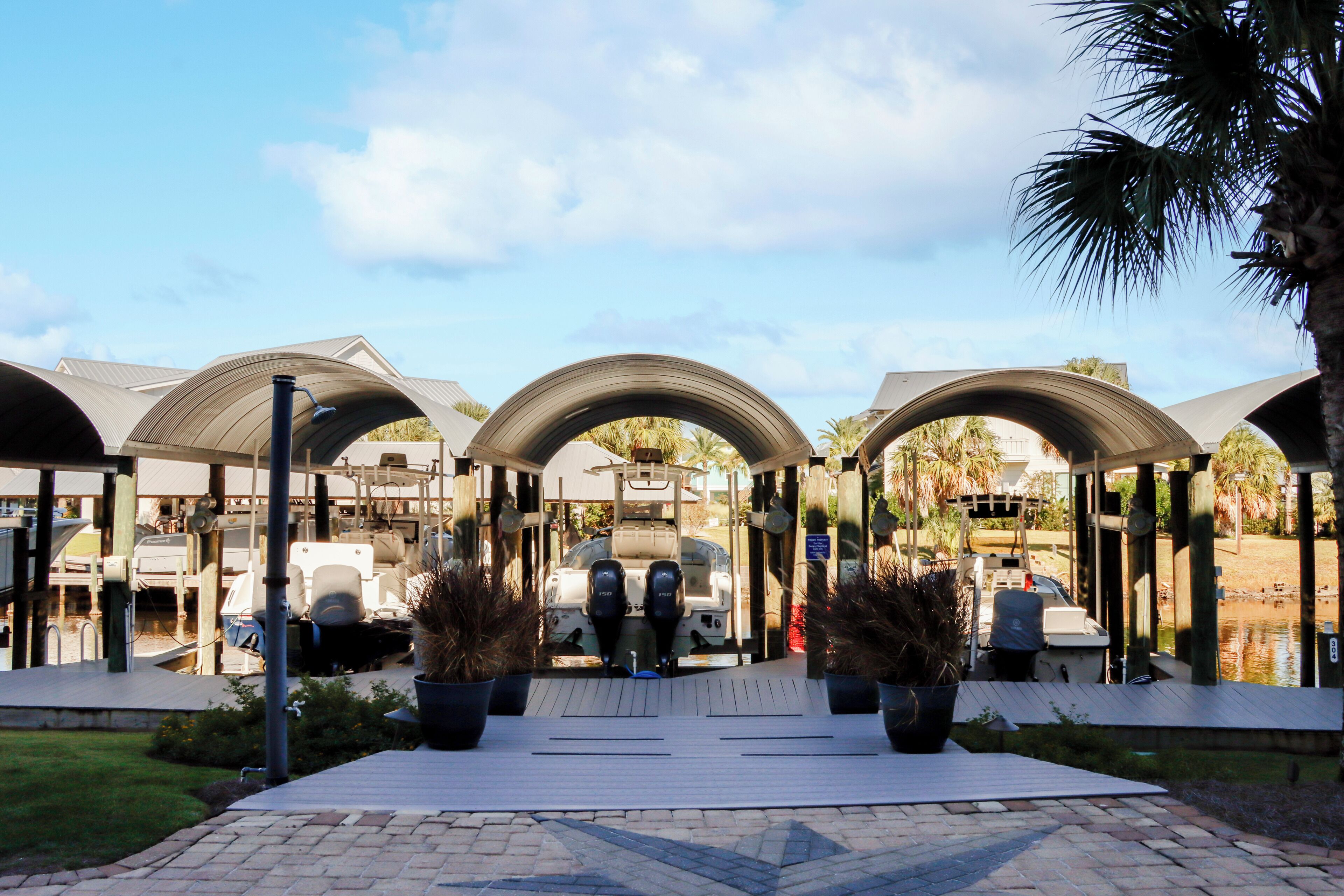 A marina with covered boat docks, a boat moored in the center, and a paved walkway leading to the docks.