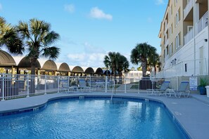 A swimming pool with lounge chairs and palm trees, surrounded by a white fence and a building with balconies. - ☀️ The Villas #302 - Pet Friendly - Canal Front ☀️ (Mexico Beach)