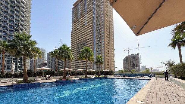 A swimming pool with lounge chairs and umbrellas, surrounded by tall buildings and palm trees. - StayShort - 1 Bed in JVC Sleeps 4 with City Views! (Jumeirah Village Circle)