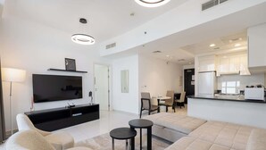 A modern living room with a flat-screen TV, sofa, and two small tables. - StayShort - 1 Bed in JVC Sleeps 4 with City Views! (Jumeirah Village Circle)