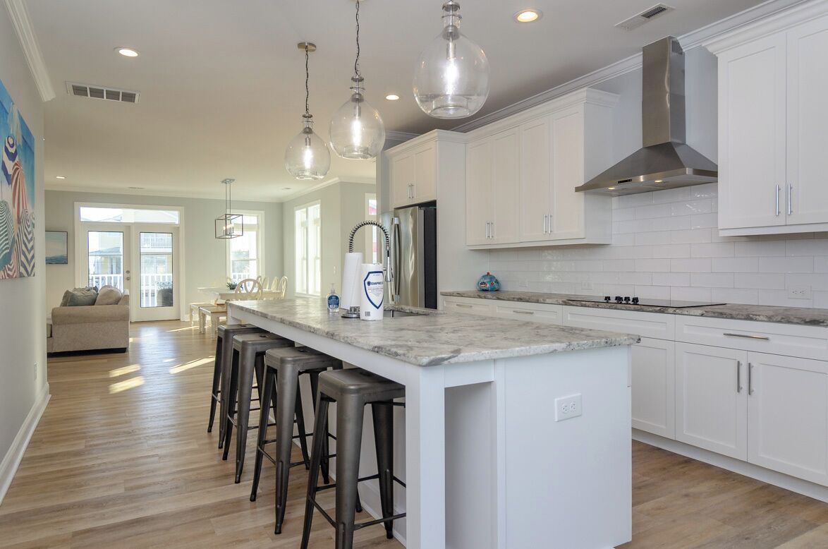 A modern kitchen with white cabinets, a large island with bar stools, stainless steel appliances, and pendant lighting.