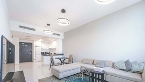 Una sala de estar moderna con un sofá seccional, una mesa de centro y un televisor. Se observa una cocina al fondo con una zona de comedor.