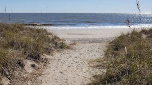 Een zandpad naar de oceaan, omgeven door gras en duinen.