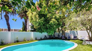 A swimming pool with a white edge, surrounded by a well-maintained lawn and trees. - Palm Paradise (Cape Town)