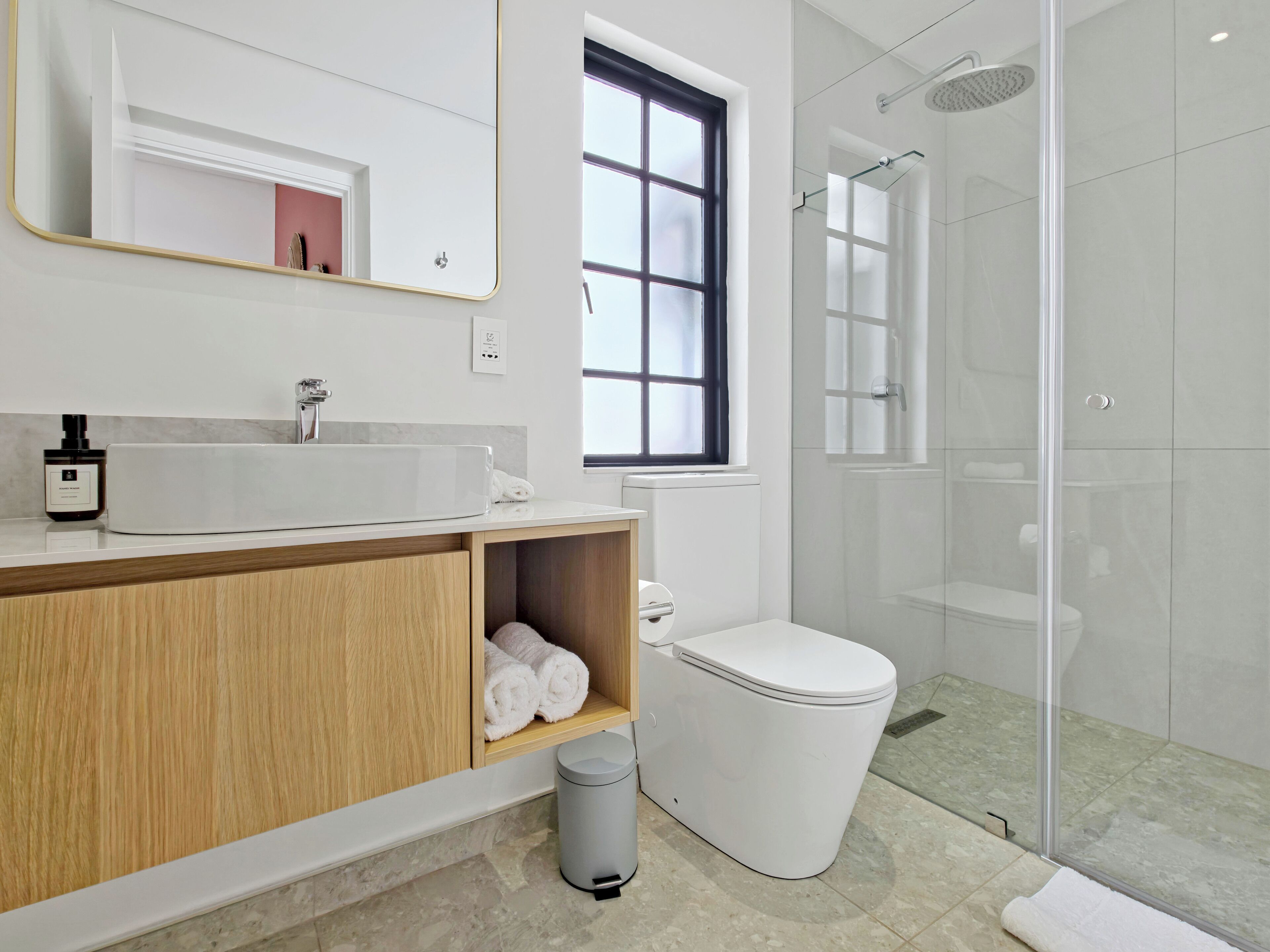 Een moderne badkamer met een wit wastafel, houten wastafelmeubel, een glazen douchecabine en een toilet.
