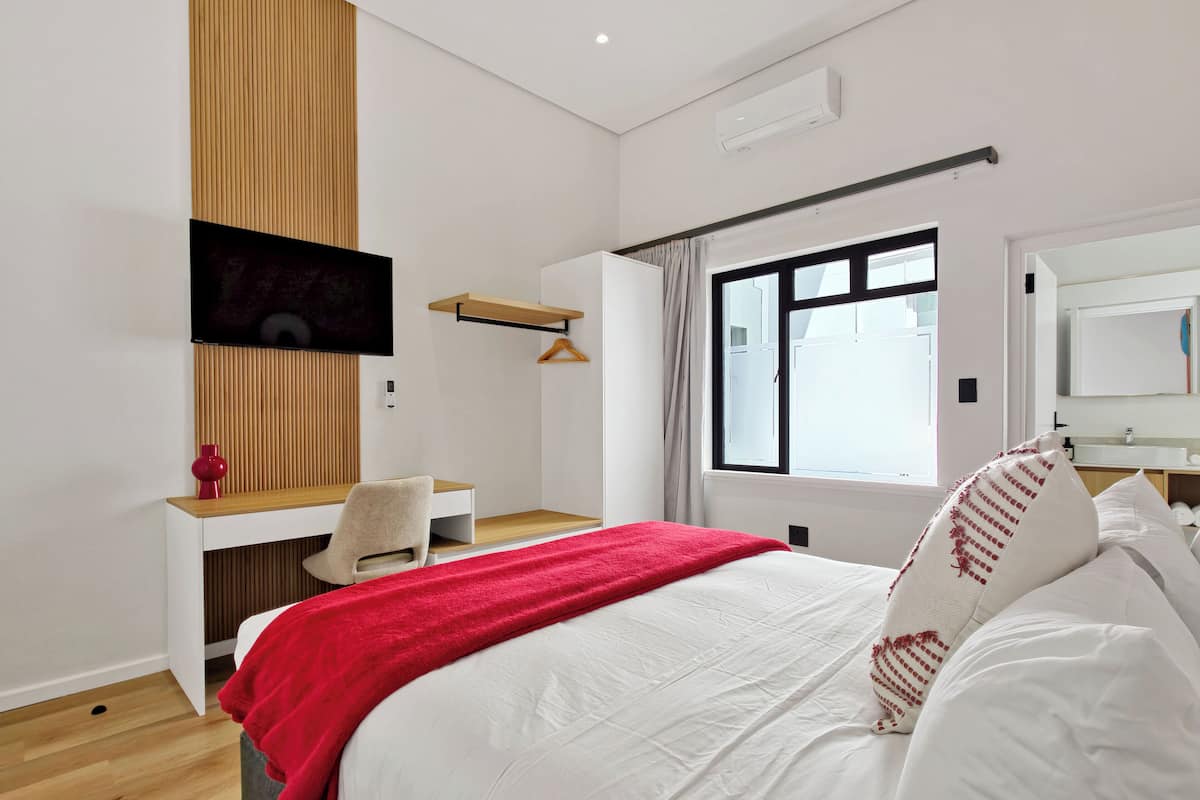 A modern bedroom with a bed, a desk, a chair, a TV, and a window.