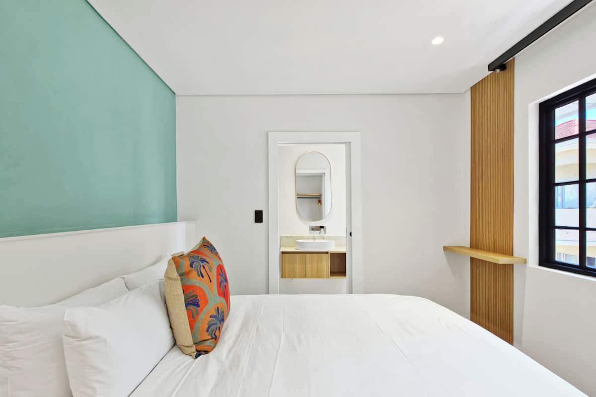 A modern hotel room with a large bed, a bathroom with a mirror and sink, and a window with a view.