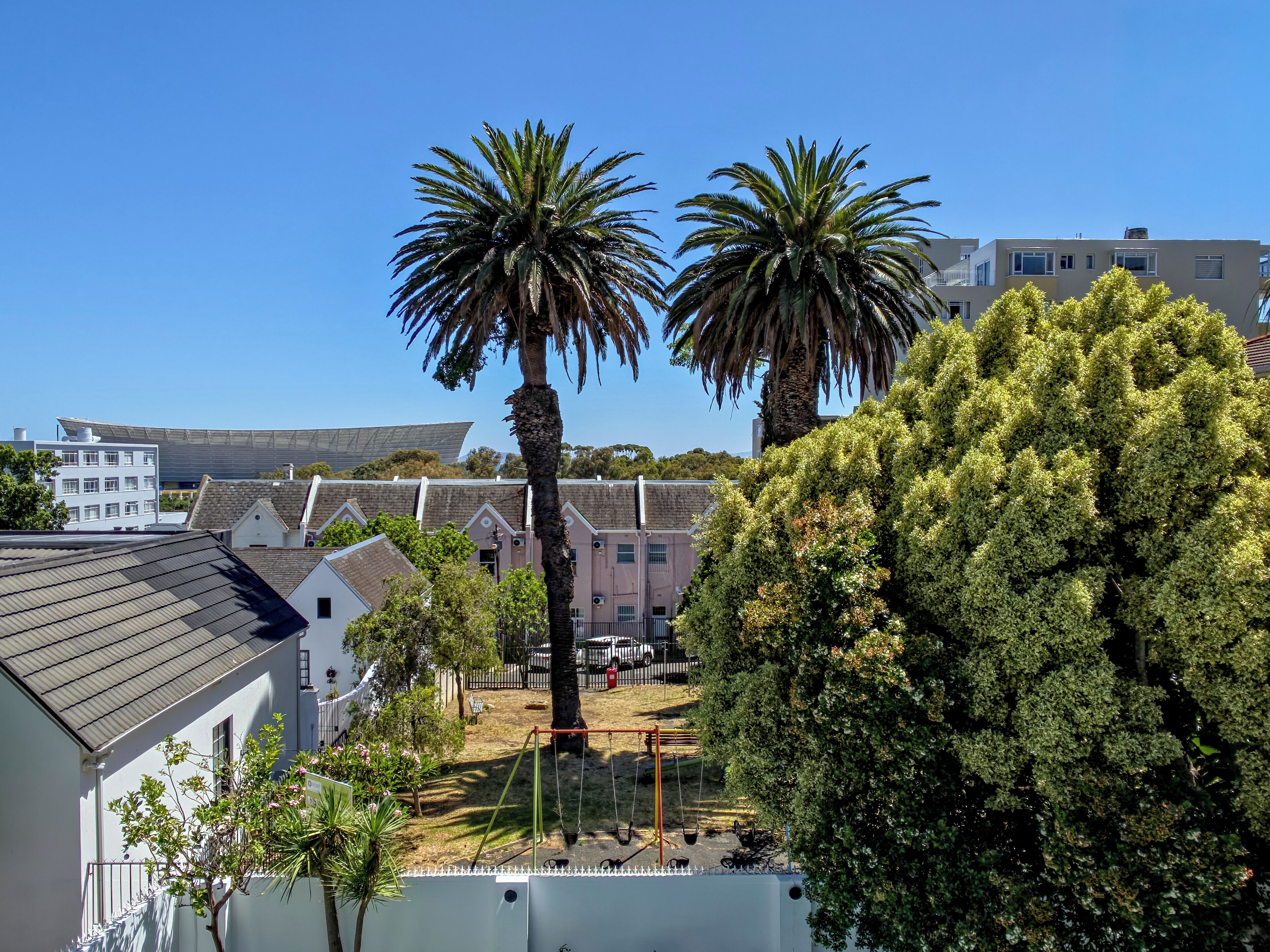 A residential area with two palm trees, a playground, and houses with sloped roofs.