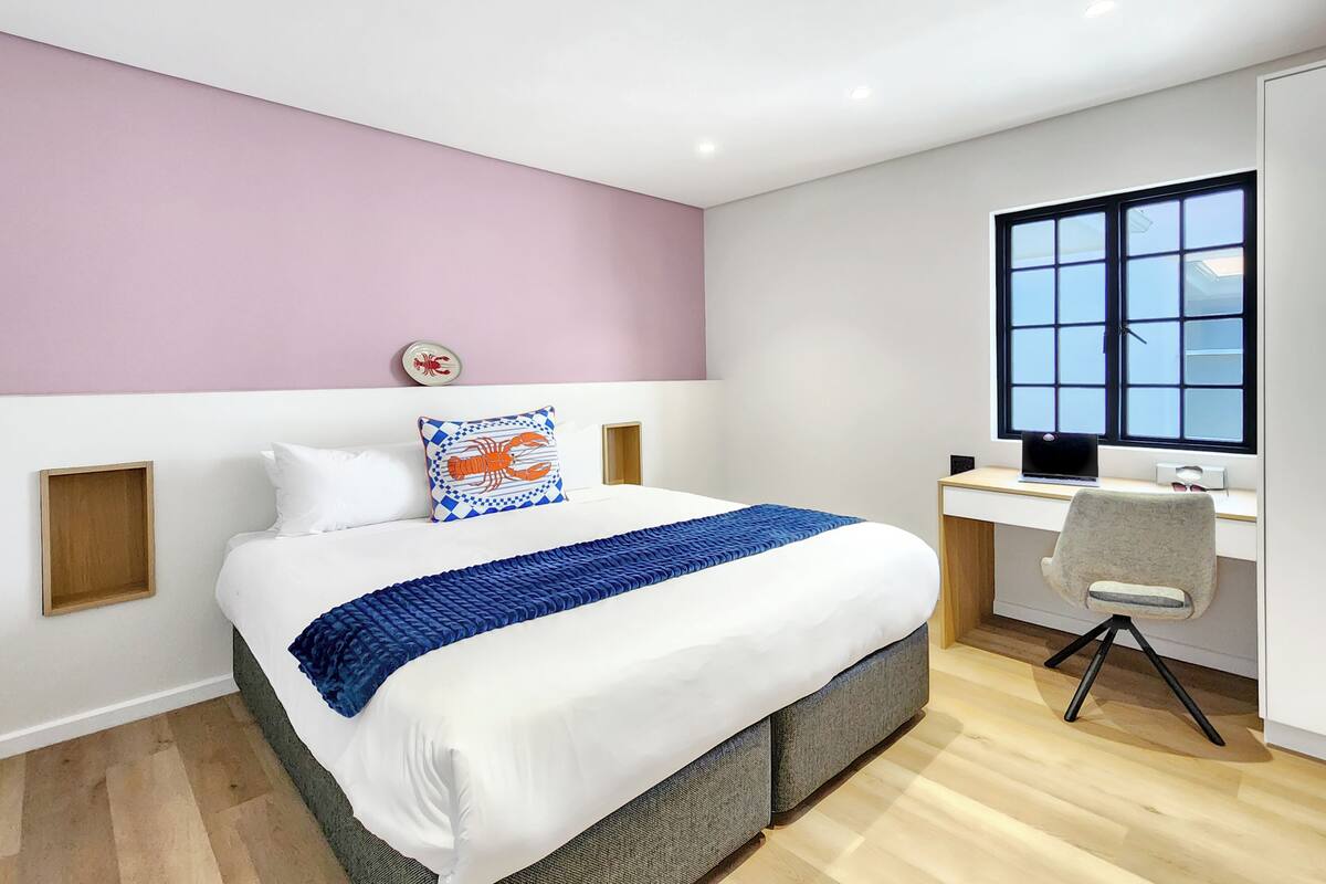 A bedroom with a bed, a desk, a chair, and a window.
