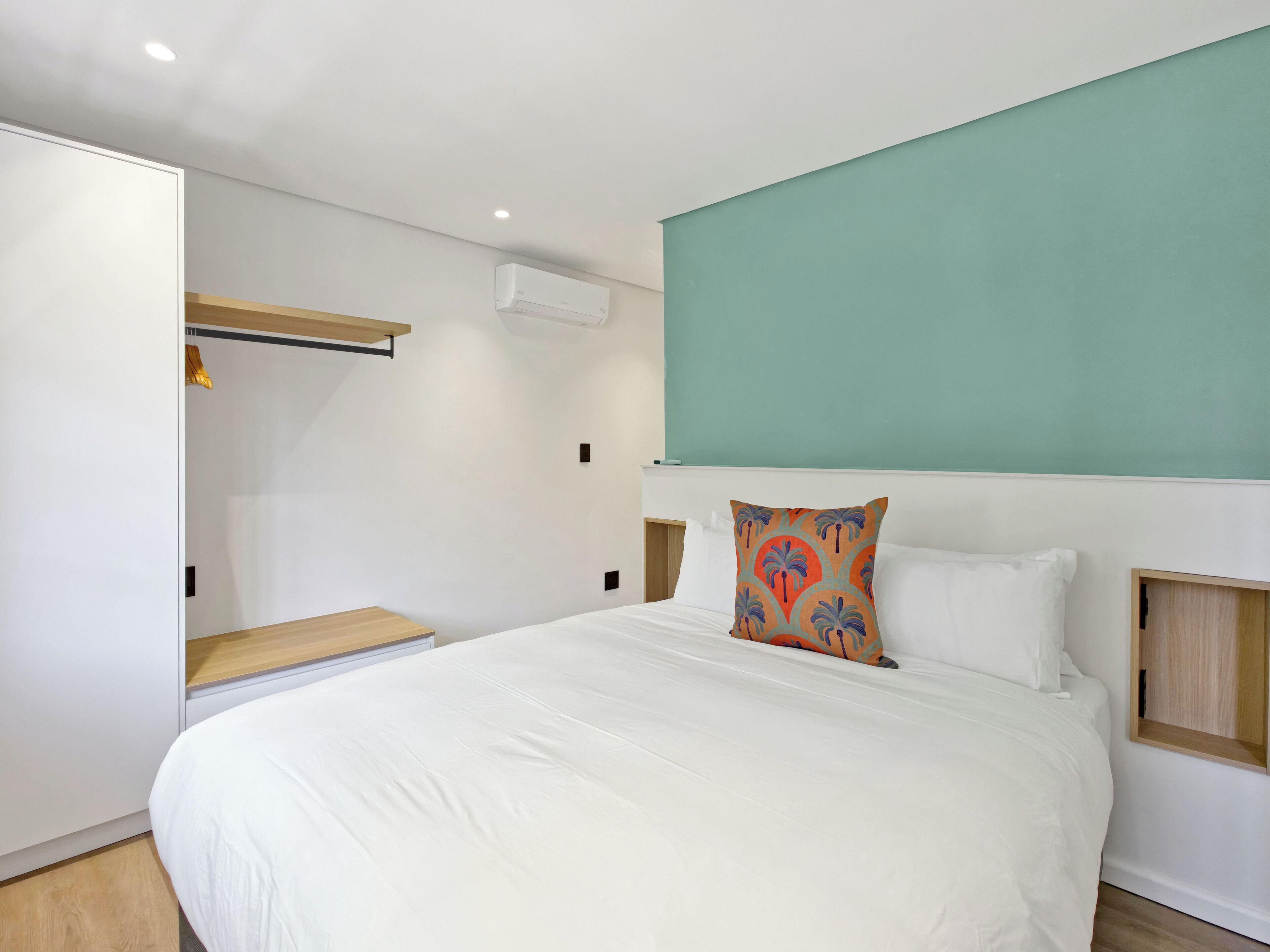 Een moderne hotelkamer met een groot bed, een garderobe, een bankje en een muur in turquoise.