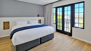 A modern bedroom with a large bed, a view through a sliding door, and a wooden floor. - Palm Paradise (Cape Town)