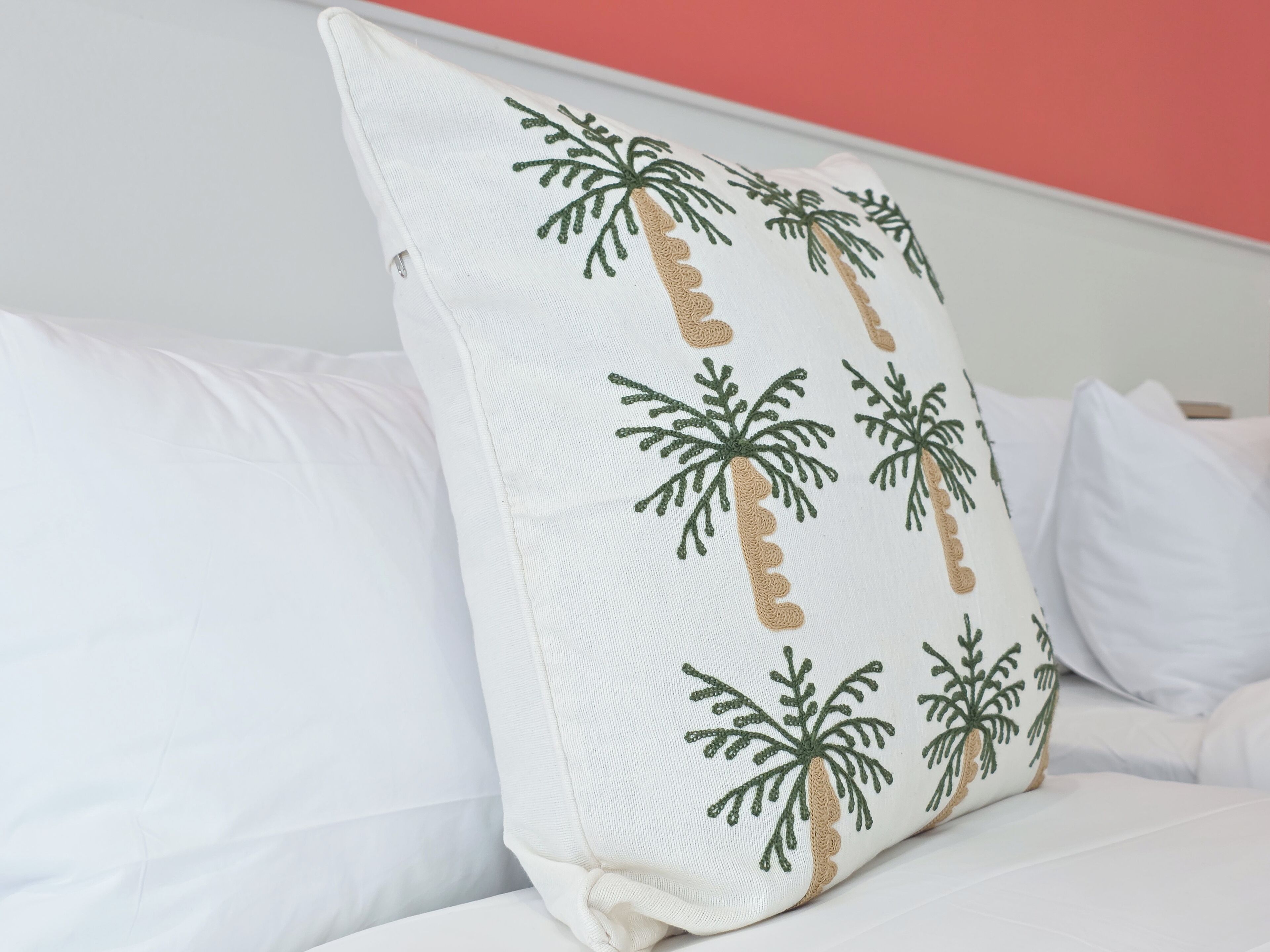 A pillow with palm tree embroidery on a bed with white bedding.
